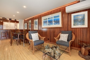 A cozy living room with wicker furniture, a glass coffee table, and framed artwork on the walls.