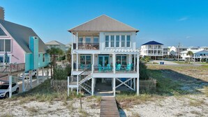 A two-story beach house with a balcony and outdoor seating area.