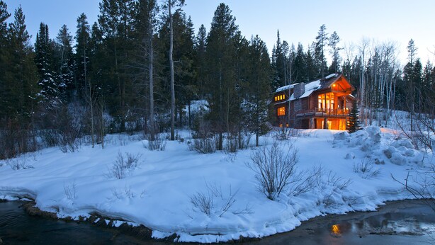 A log cabin with a porch and multiple windows, surrounded by a snowy landscape and dense forest. - Blue Winged Olive Log Cabin Magnificence in Victor, ID w/ A/C, Borders Forest (Victor)