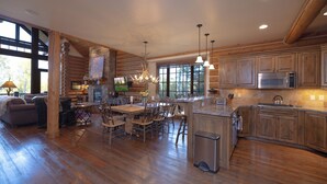 A spacious kitchen with wooden cabinets, a large island, and a dining area with chairs and a table. - Blue Winged Olive Log Cabin Magnificence in Victor, ID w/ A/C, Borders Forest (Victor)