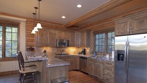 A spacious kitchen with wooden cabinets, stainless steel appliances, and a bar area with stools. - Blue Winged Olive Log Cabin Magnificence in Victor, ID w/ A/C, Borders Forest (Victor)