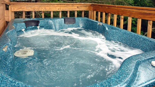 Un jacuzzi con una terraza de madera y vistas a árboles al fondo.