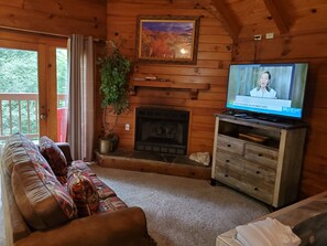 A cozy cabin interior with a wooden fireplace, a television, a sofa, and a potted plant.