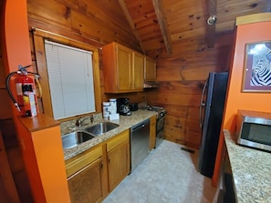 A compact kitchen with wooden cabinets, a granite countertop, a stainless steel sink, a stove, and a refrigerator.