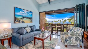 A living room with a sofa, coffee table, and a view of the ocean through a sliding glass door. - Maui Vista #1-418 Ocean View/Pickle Ball Courts, Close to the Beach, Wifi (Kihei)