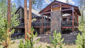 A log cabin with a large deck, surrounded by tall trees.