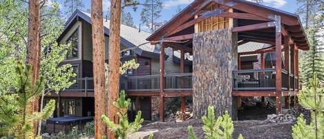 A log cabin with a large deck, surrounded by tall trees.