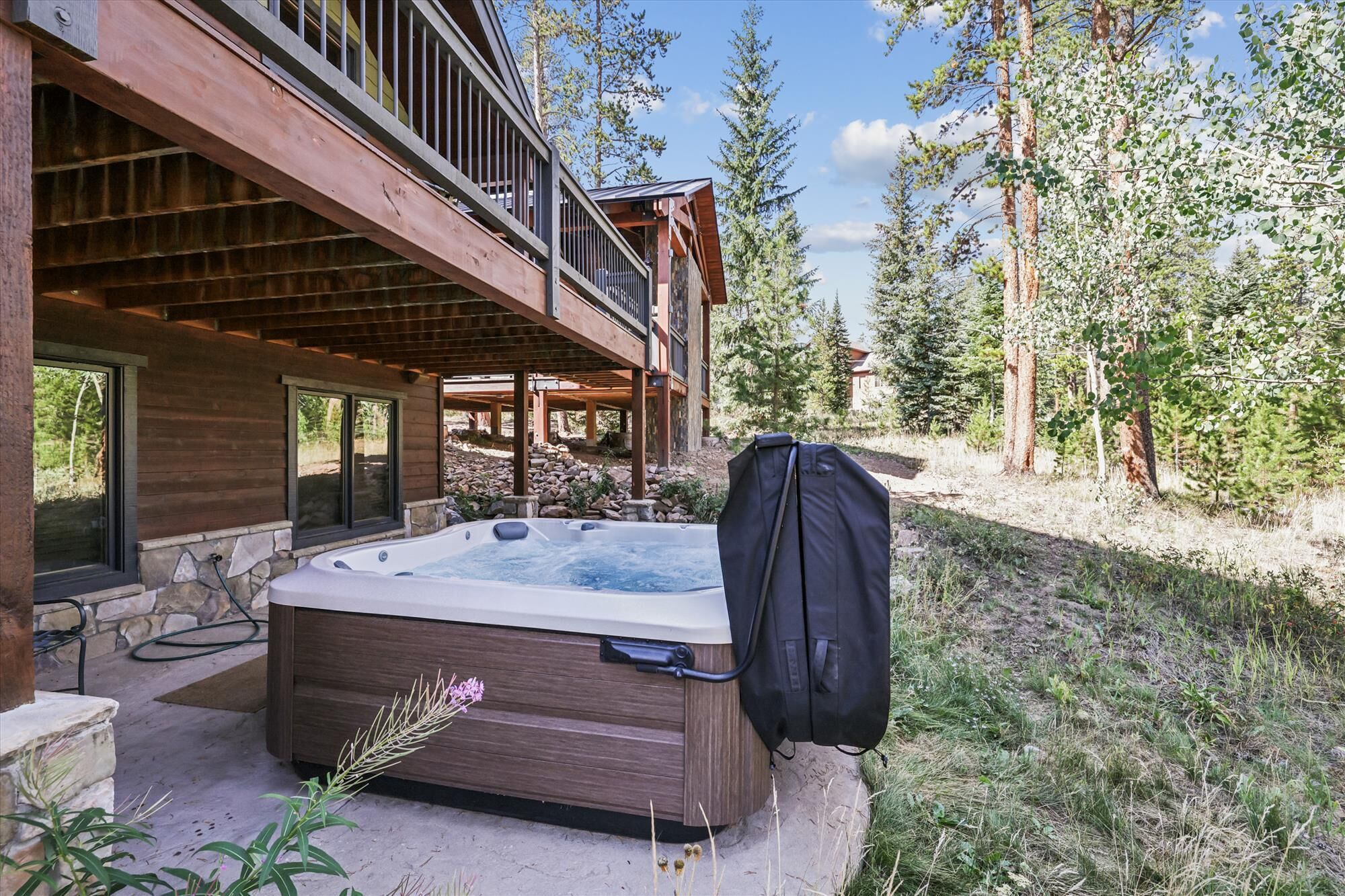 Une cabane en bois dotée d’un bain à remous et d’un espace barbecue couvert, le tout entouré d’arbres.