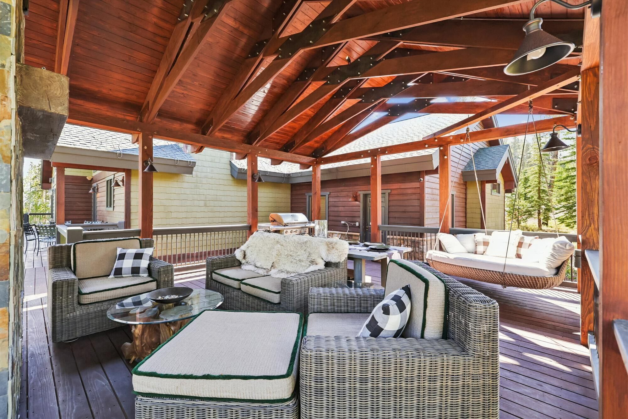 A covered outdoor patio with wicker furniture, a grill, and a view of the surrounding area.