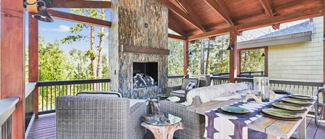 A covered outdoor patio with wicker furniture, a stone fireplace, and a dining table set for a meal.