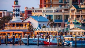 Un hotel frente al agua con un faro, varias zonas de restauración y barcos amarrados.