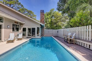 A backyard with a swimming pool, deck chairs, and a wooden fence.