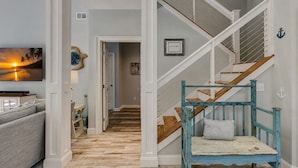 A hallway with a wooden floor, a staircase with blue railings, and a wall-mounted television. - 5 Green Heron - 5th Row Ocean Home in Sea Pines (Hilton Head Island)