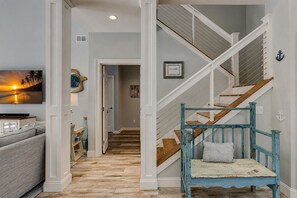 A hallway with a wooden floor, a staircase with blue railings, and a wall-mounted television.