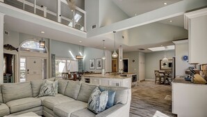 A spacious living area with a large L-shaped sofa, a dining table, and a kitchen area with a central island. - 5 Green Heron - 5th Row Ocean Home in Sea Pines (Hilton Head Island)