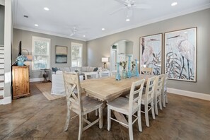 Un espace repas avec une table en bois et des chaises blanches, entouré de murs gris et d’œuvres d’art.