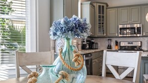 A dining table with a decorative glass vase and rope handles, set in a kitchen with wooden cabinets and a chandelier.