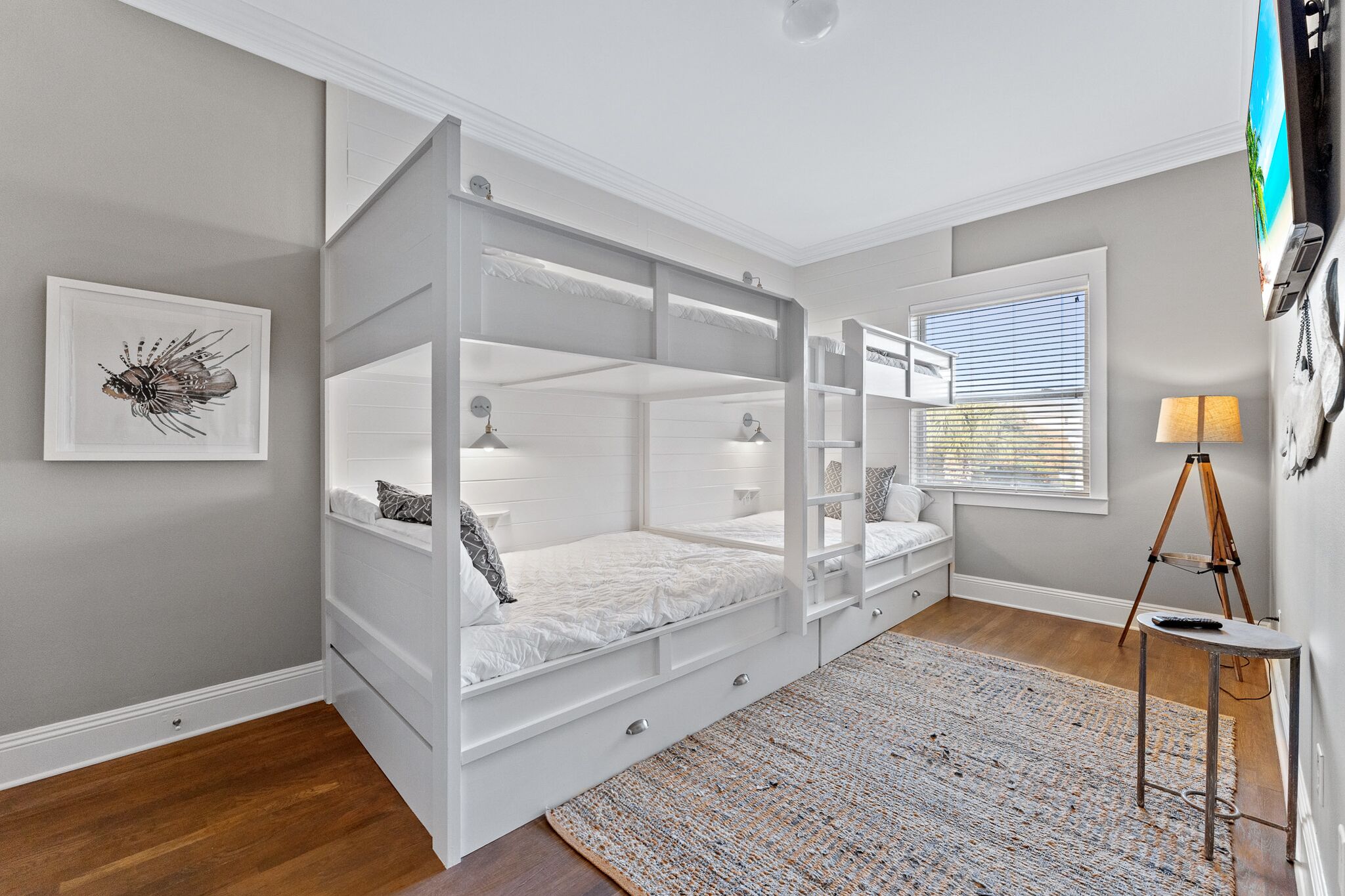 Une chambre avec un lit superposé, un tableau encadré au mur, une fenêtre avec des stores, une lampe et un trépied.