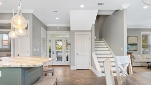 A spacious kitchen with a marble island, a dining area with wooden chairs, and a staircase leading to another level.