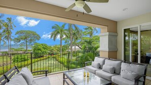 A balcony with a glass table, grey sofa, and a ceiling fan. - Ocean Front Luxury Condo, close to pool area! (Playa Herradura)