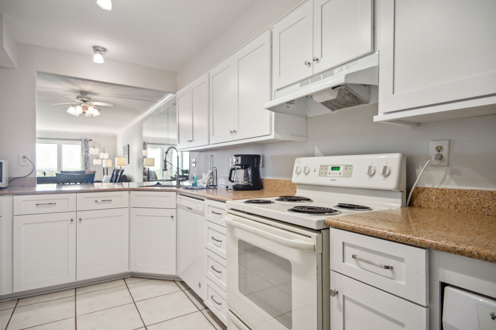 A modern kitchen with white cabinets, a granite countertop, a stove, and a ceiling fan.