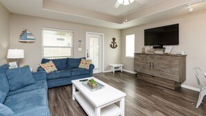 A living room with a blue sofa, a white coffee table, a wooden cabinet, and a ceiling fan. - Pet-Friendly Beach Retreat | Heated Pool & Walk to Beach (Corpus Christi)
