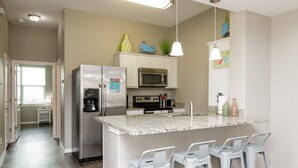 A modern kitchen with a central island, bar stools, stainless steel appliances, and decorative items on the wall. - Pet-Friendly Beach Retreat | Heated Pool & Walk to Beach (Corpus Christi)
