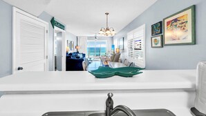 A modern kitchen with a white countertop, a dining area with a green table runner, and a view of the ocean through large windows. - Recently updated 2 bedroom-Beach Front Condo-Sleeps 6-Beach Service Included!! (Fort Walton Beach)