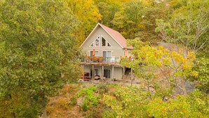 A two-story house with a balcony, surrounded by trees with autumn foliage. - All Decked Out: Beautiful Chalet-style Seneca Lake Home! (Burdett)
