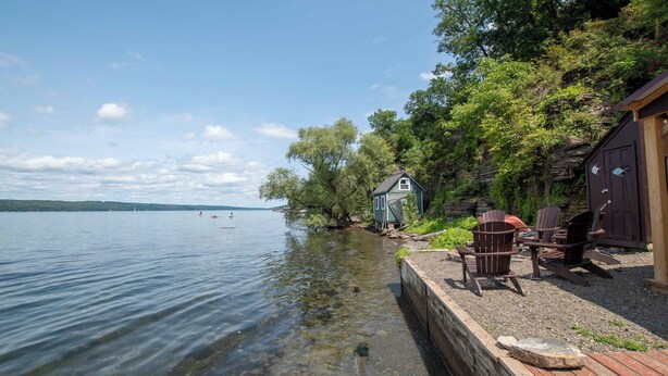 A lakeside cabin with a dock, outdoor seating, and a small shed. - All Decked Out: Beautiful Chalet-style Seneca Lake Home! (Burdett)