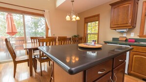 A kitchen with wooden cabinets, a large island, and a dining area with wooden chairs and a table. - All Decked Out: Beautiful Chalet-style Seneca Lake Home! (Burdett)