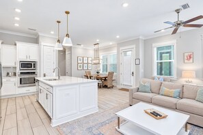 Una cocina moderna con armarios blancos, una isla central, iluminación colgante y una zona de comedor con mesa y sillas.