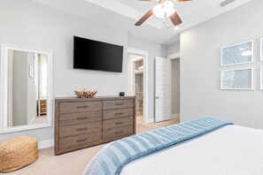 A bedroom with a bed, a dresser, a television, and a ceiling fan.