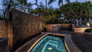 A swimming pool with a tiled deck, surrounded by palm trees and a stone wall.