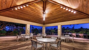 An outdoor patio with round tables and chairs, a wooden ceiling, and barbecue grills.