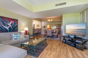 A living room with a sofa, coffee table, and a TV. There is a dining area with chairs and a table.