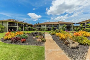 A hotel with a central pathway, surrounded by landscaped gardens with various plants and a clear sky.