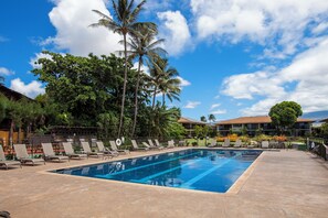 A swimming pool with lounge chairs, palm trees, and a building in the background.