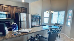 A kitchen with wooden cabinets, stainless steel appliances, a granite countertop, and a dining area with a chandelier.
