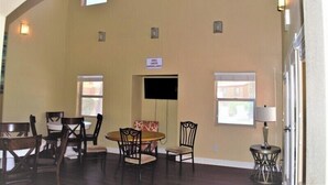 A dining area with a round table and chairs, a sofa, and a sign indicating surveillance.
