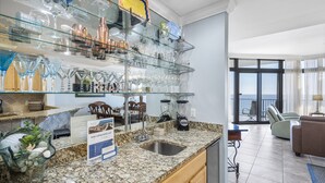 A kitchen with granite countertops, a glass display shelf, and a dining area with a view. - The Oasis At Orange Beach 808 by Liquid Life (Orange Beach)