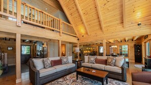 A spacious living area with a high ceiling and wooden beams, featuring two sofas with patterned cushions, a coffee table, and a patterned rug.