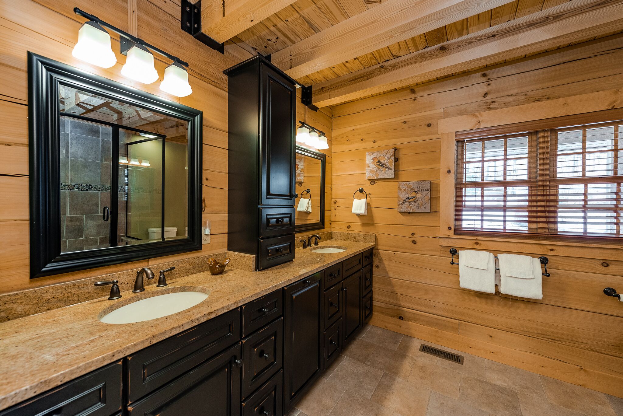 A wooden cabin bathroom with two sinks, a large mirror, and wooden walls.