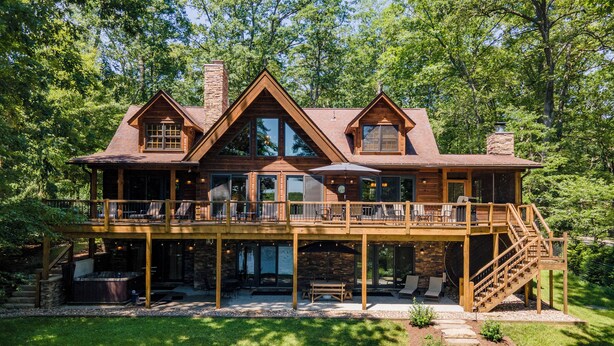 A large, two-story wooden house with a deck, outdoor seating, and a hot tub.