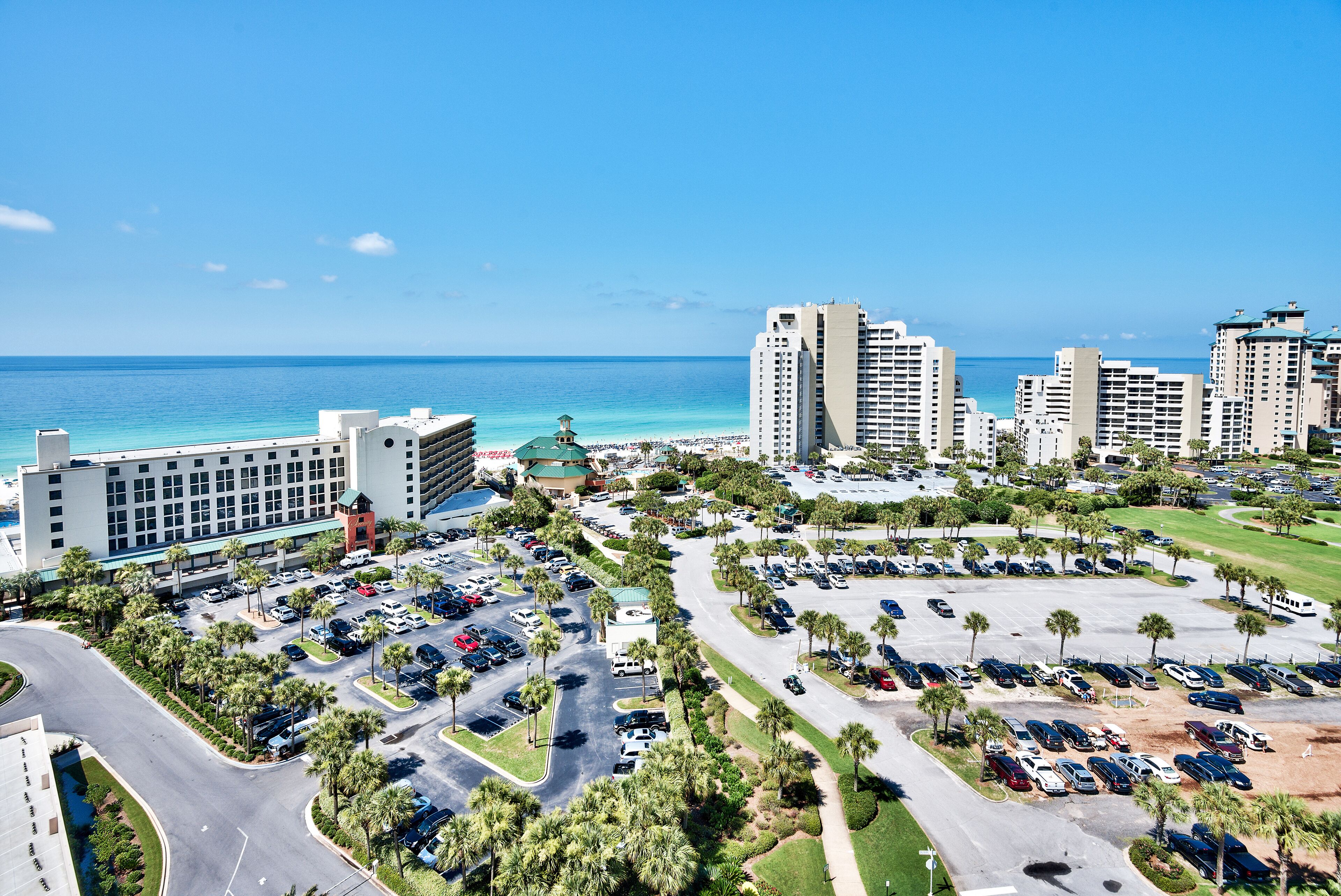 A hotel with multiple parking lots, a large building with a green roof, and a view of the ocean.