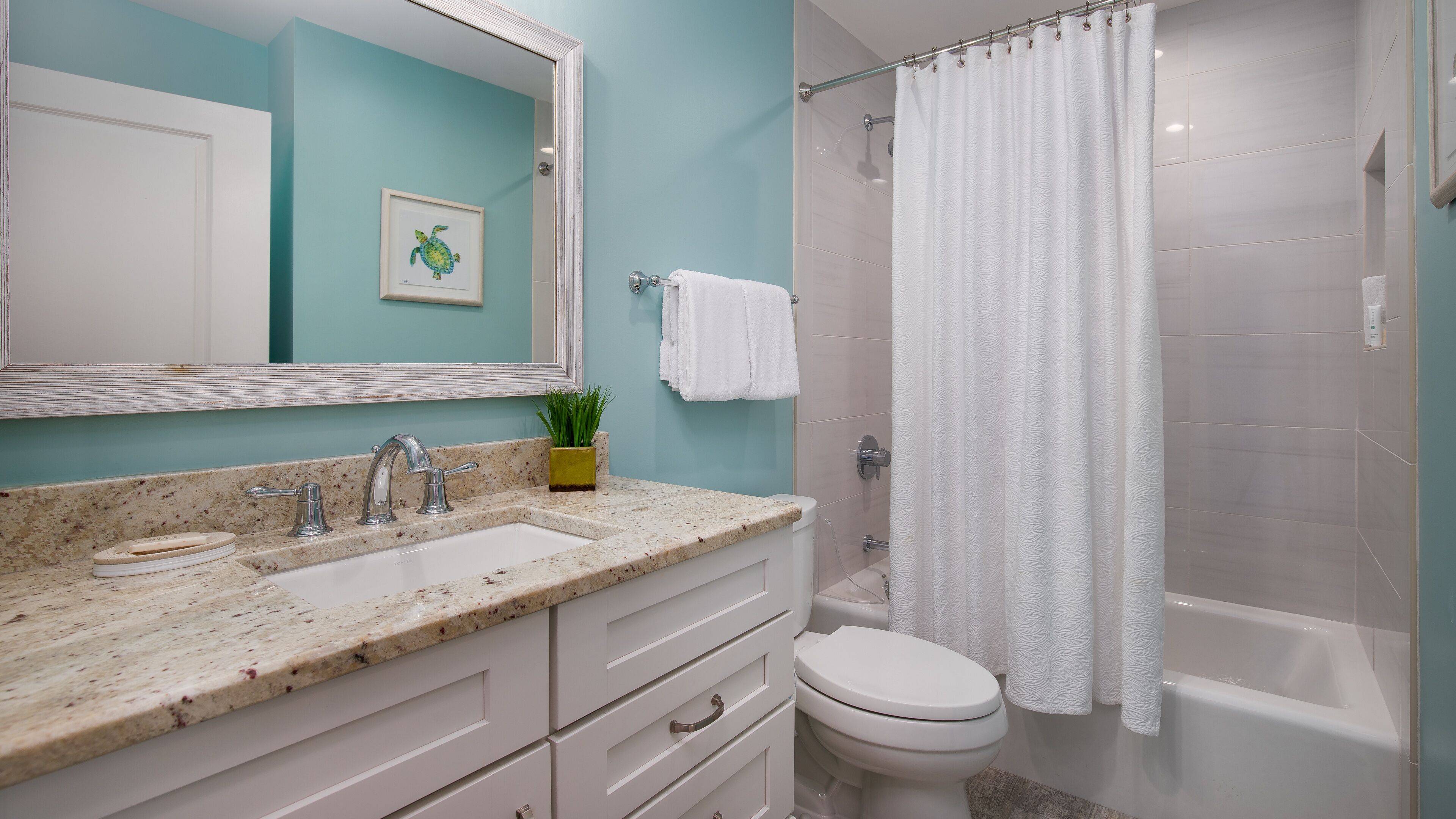 Un baño con encimera de mármol, dos lavamanos, un inodoro y una ducha con cortina blanca.