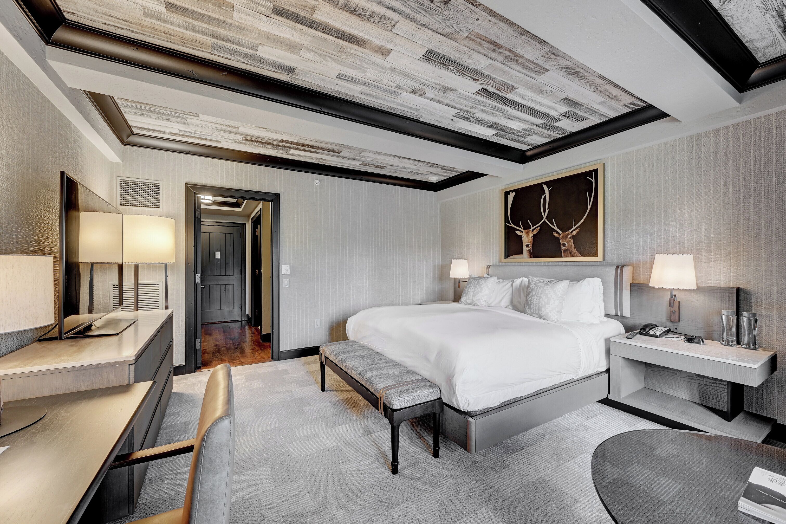 A modern hotel room with a large bed, bedside tables, a desk, and a bench.