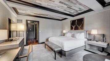 A modern hotel room with a large bed, bedside tables, a desk, and a bench.