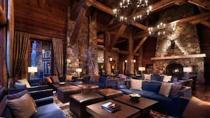 Ein rustikal eingerichteter Innenraum im Chalet-Stil mit Kamin aus Stein, mehreren Sitzbereichen und einem Chandelier.