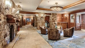 Eine großzügige Lobby mit Steinwänden, Holzvertäfelung und verschiedenen Sitzbereichen, darunter Sessel und eine Couch.